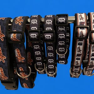 May include: A set of six dog collars with different designs featuring the Detroit Tigers logo. The collars are black with white and orange accents. The collars are made of a durable nylon material and have a metal buckle.