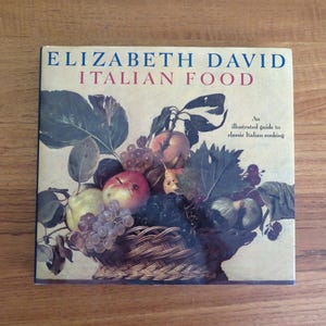 May include: A square cookbook titled Italian Food by Elizabeth David, featuring a still life illustration of a woven basket filled with various fruits including grapes, apples, and pears, with green leaves and the text An illustrated guide to classic Italian cooking.