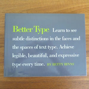 以下が含まれることがあります： 「Better Type」というタイトルの本で、灰色の表紙に緑と白の文字が書かれています。テキストには「テキストタイプの顔とスペースの微妙な違いを見てください。毎回読みやすく、美しく、表現力豊かなタイプを実現します。BETTY BINNSによる」と書かれています。