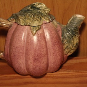 Może przedstawiać: Ceramiczny czajnik w kształcie fioletowej dyni z zielonymi liśćmi na pokrywce i wylewce.
