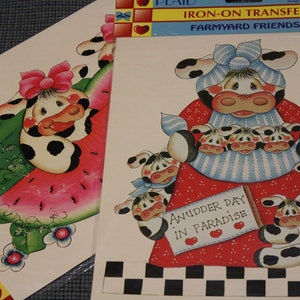 Puede incluir: Hoja de transferencia termoadhesiva con una vaca de dibujos animados con un vestido rojo y blanco y una camisa a rayas azul y blanca. La vaca sostiene tres vacas más pequeñas en sus brazos. El texto "Anudder Day In Paradise" está en un cartel delante de la vaca. La hoja de transferencia es para usar en telas oscuras o claras.