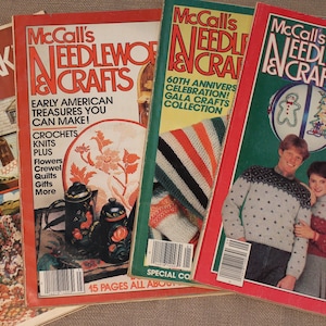 May include: Four vintage McCall's Needlework & Crafts magazines with colourful covers featuring various craft projects. The covers include a miniature house, a teapot, a knitted scarf, a gingerbread man ornament, and a Christmas ornament.