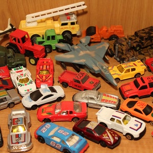 May include: A collection of toy vehicles, including a red tractor, a blue and white airplane, a yellow fire truck, a green jeep, a camouflage military truck, and several cars in various colors.