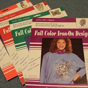 May include: Four packages of iron-on designs for clothing. Each package features a different design and a model wearing a shirt with the design. The text on the packages reads "Full Color Iron-On Design" and "Just iron on and wear... NO PAINTING REQUIRED!"