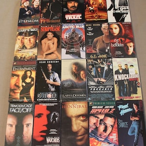 May include: A collection of VHS movie tapes, including titles like "Stepmom", "Unforgiven", "Crossfire Trail", "Arctic Blue", "Hart's War", "Striptease", "Eye of the Beholder", "Entrapment", "Outland", "Last of the Dogmen", "Freejack", "Knockaround Guys", "Face/Off", "Hannibal", "Speed 2: Cruise Control", "Road House", and "Watchers".