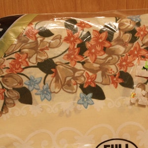 May include: A cream-colored floral bed sheet with a brown, green, and orange floral pattern. The sheet is packaged in plastic and has a "Full" size label. The packaging also has the text "Homesteader" on it.
