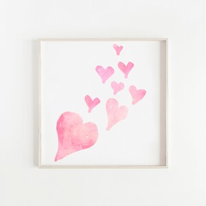 May include: A framed print with a watercolor painting of pink hearts. The hearts are arranged in a cluster, with the largest heart at the bottom and the smaller hearts floating upwards.