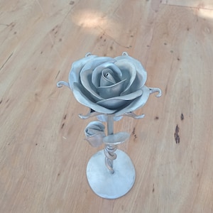 May include: A silver metal rose sculpture with a twisted stem and a round base. The rose has a detailed design with multiple petals.