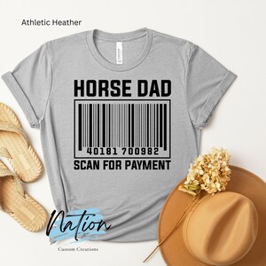 Könnte beinhalten: Graues T-Shirt mit dem Text "HORSE DAD" und einem Barcode mit der Nummer "40181 700982" und dem Text "SCAN FOR PAYMENT" darunter.