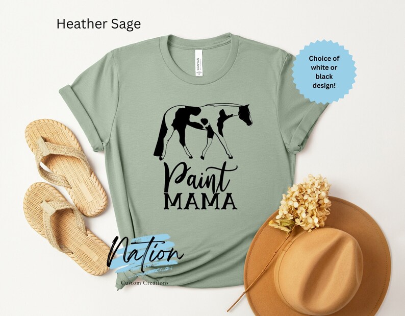 K&ouml;nnte beinhalten: Heather Sage gr&uuml;nes T-Shirt mit einem schwarzen und wei&szlig;en Paint-Pferd- und Reiter-Motiv. Der Text "Paint Mama" ist unter dem Motiv gedruckt. Das Shirt ist in Wei&szlig; oder Schwarz erh&auml;ltlich.