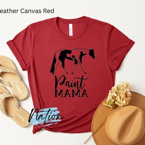 K&ouml;nnte beinhalten: Rotes T-Shirt aus Heather-Canvas mit einer schwarzen Silhouette eines Paint-Pferdes und eines Reiters. Der Text "Paint Mama" ist unter dem Bild gedruckt.