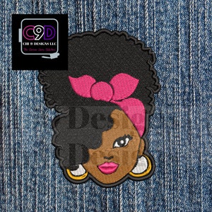 May include: Embroidered patch featuring a woman with an afro hairstyle, wearing a pink headband and large gold hoop earrings. The woman has brown skin and is looking directly at the viewer.