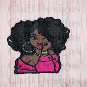 May include: Embroidered patch of a woman with black curly hair, wearing a pink shirt and green earrings. She is winking and has her hand on her chin.