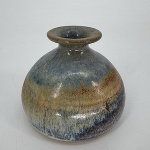 May include: A handcrafted ceramic vase with a rounded body and a narrow neck. The vase features a blend of blue, brown, and beige hues, creating a unique, textured appearance. The opening is approximately 2 inches in diameter.