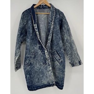 May include: A vintage acid wash denim jacket with a long, open design. The jacket features a shawl collar, two front pockets, and a light blue and white marbled pattern. The jacket is hanging on a wooden hanger.