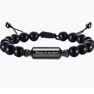 May include: Black beaded bracelet with a black metal charm engraved with the words "Always in my heart".