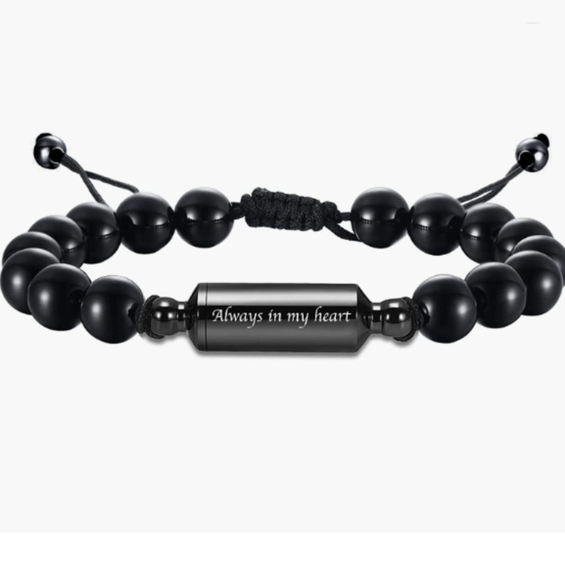 May include: Black beaded bracelet with a black metal charm engraved with the words "Always in my heart".