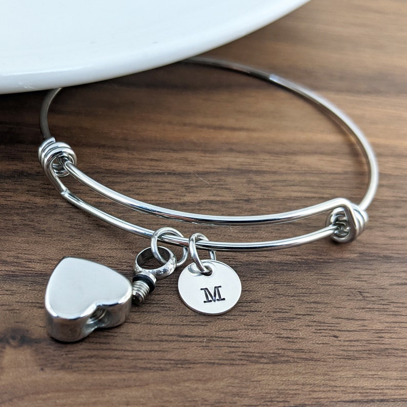 Pu&ograve; includere: Un braccialetto rigido in argento con un ciondolo a forma di cuore e un ciondolo rotondo con la lettera "M" incisa.