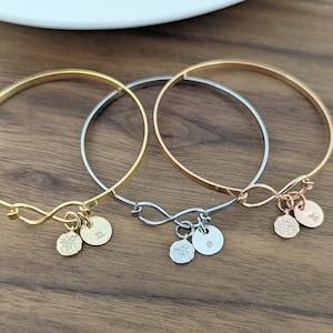 May include: Three infinity symbol charm bracelets in gold, silver, and rose gold. Each bracelet has a small charm with a sparkling stone and a letter.