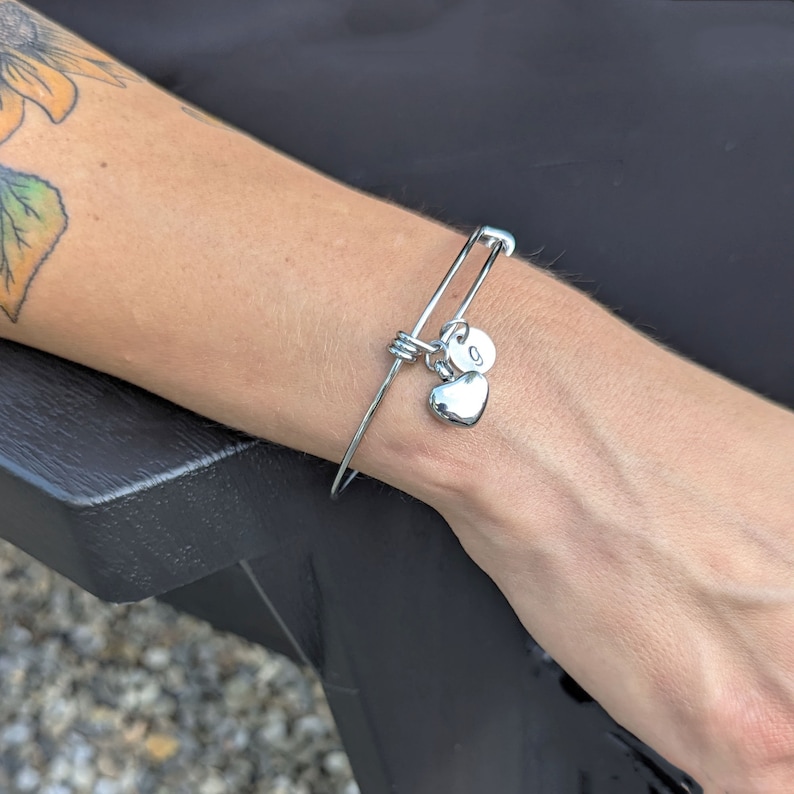 Pu&ograve; includere: Un braccialetto rigido in argento con un ciondolo a forma di cuore e un ciondolo con la lettera 'G'.