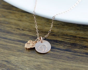Pode incluir: Colar de ouro rosa com um pequeno pingente de pata e um pingente de disco maior com a letra D gravada.