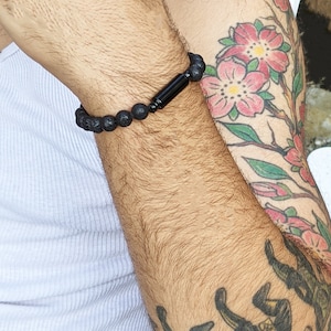May include: A black beaded bracelet with a black metal accent. The bracelet is on a person's wrist.