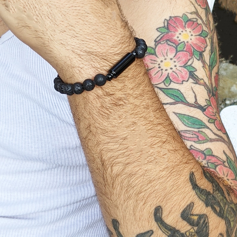 May include: A black beaded bracelet with a black metal accent. The bracelet is on a person's wrist.