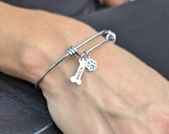 May include: Silver expandable bracelet with a charm in the shape of a bone with the name "Bella" engraved on it and a paw print charm.