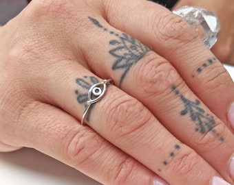 May include: A silver ring with an evil eye design. The ring is on a finger with a tattoo.