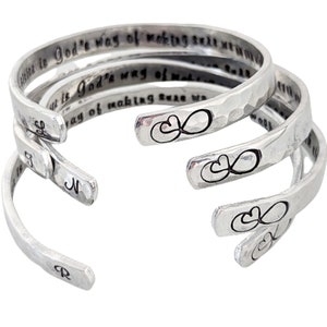 May include: Set of three silver bracelets with a hammered finish. Each bracelet features an infinity symbol with two hearts and an inscription that reads "God's way of making sure we never walk alone".