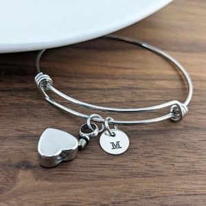 Pu&ograve; includere: Braccialetto rigido in argento con un ciondolo a forma di cuore e un ciondolo rotondo con la lettera "M" incisa.