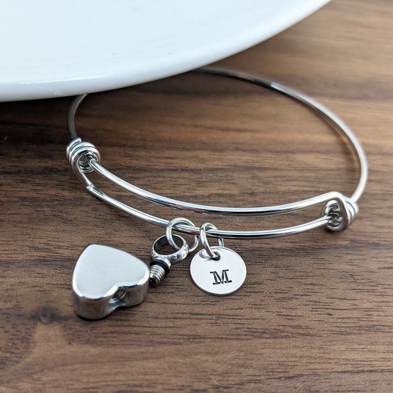 Pu&ograve; includere: Braccialetto rigido in argento con un ciondolo a forma di cuore e un ciondolo rotondo con la lettera "M" incisa.