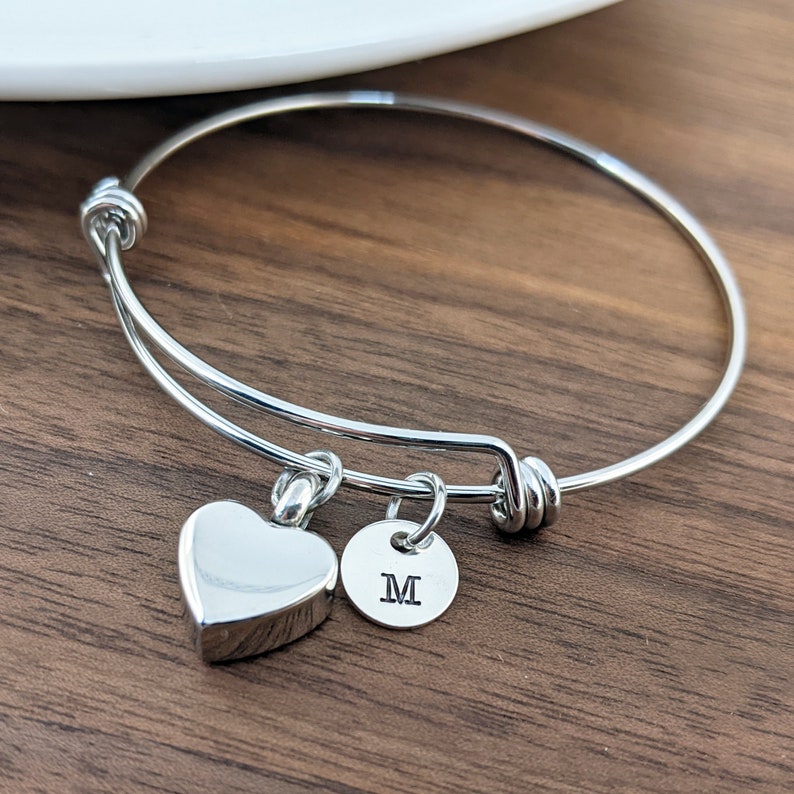 Pu&ograve; includere: Un braccialetto rigido in argento espandibile con un piccolo ciondolo a forma di cuore e un ciondolo rotondo con la lettera "M" incisa.