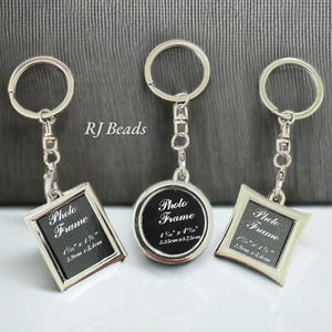 May include: Three silver-toned metal photo frame keychains with split rings and lobster clasps. The frames are square, round, and diamond-shaped, each containing a black insert with the text Photo Frame and dimensions in inches and cm.