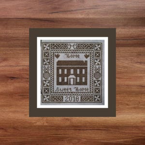 Puede incluir: Un patrón de punto de cruz marrón y blanco con una casa, corazones y el texto "Home", "Sweet Home" y "2018".