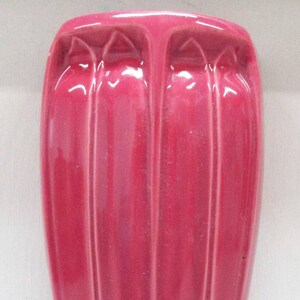 May include: A pink ceramic wall vase with a unique, fluted design. The vase is shaped like a teardrop and has a smooth, glossy finish.