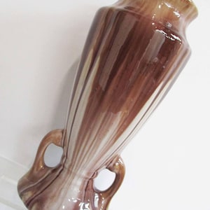 May include: A brown and white striped ceramic vase with two handles. The vase has a glossy finish and a unique swirl pattern.
