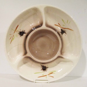 May include: A white ceramic serving dish with four sections and a central dip bowl. The dish has a brown glaze with a stylised design of black and brown lines and dots.