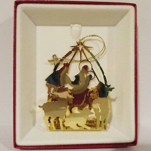 Op de afbeelding: Gouden metalen kerstversiering die de kerststal voorstelt. De versiering heeft een ster, een kribbe, Maria, Jozef, het kindje Jezus en schapen.
