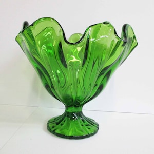 Op de afbeelding: Een groene glazen kom met een gegolfde rand en een voet. De kom heeft een golvend, getextureerd ontwerp.