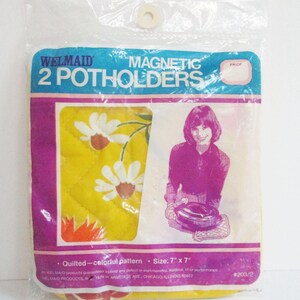 May include: A package of two Welmaid magnetic potholders in a clear plastic bag. The packaging features the text 2 POTHOLDERS, a graphic of a person holding a pot, and states the size as 7 inches by 7 inches. The potholders have a yellow floral pattern.
