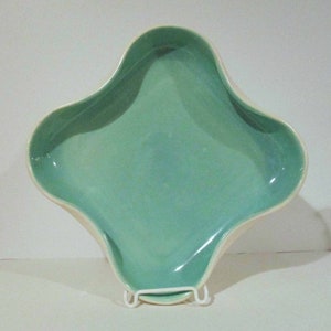 May include: A light green ceramic serving dish with a unique, four-pointed star shape. The dish has a smooth, glossy finish and a slightly raised rim.