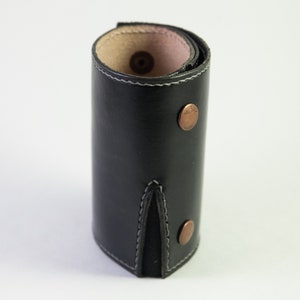 May include: A black leather key holder with a stitched seam and two copper rivets. The key holder is rolled up and has a pink lining.