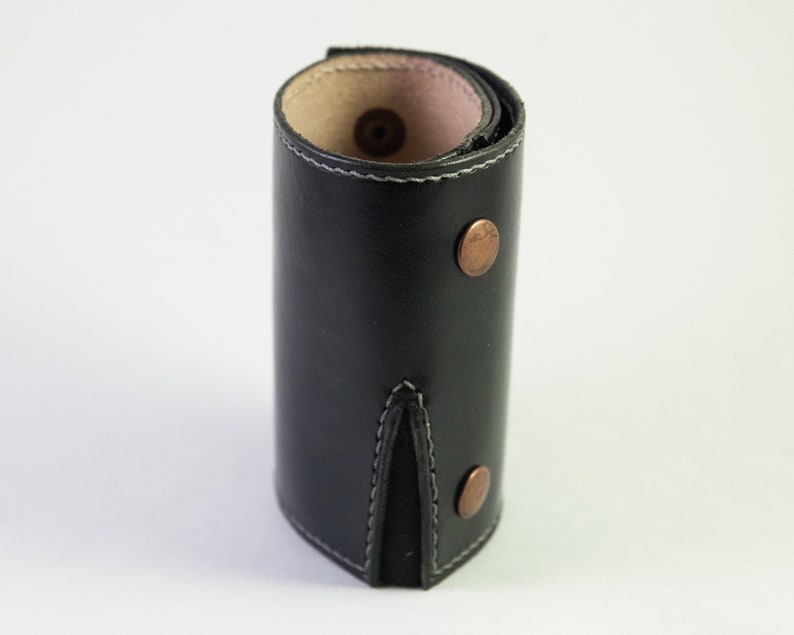 May include: A black leather key holder with a stitched seam and two copper rivets. The key holder is rolled up and has a pink lining.