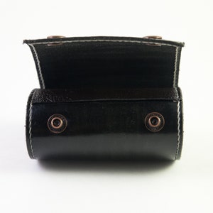May include: A black leather roll-up case with metal snaps. The case is open and the inside is lined with black fabric.