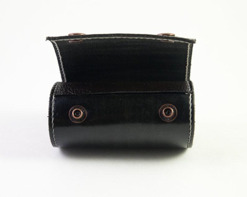 May include: A black leather roll-up case with metal snaps. The case is open and the inside is lined with black fabric.