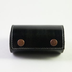 May include: A black leather roll-up case with two copper rivets. The case is closed and has a white stitch around the edges.