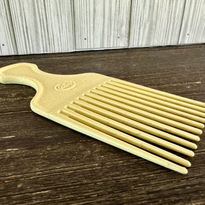 May include: A yellow plastic comb with a wide handle and a row of teeth. The comb has the word "Goody" printed on the handle.