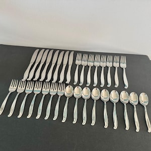 May include: A large set of stainless steel flatware including seven dinner knives, eight dinner forks, seven salad forks, and nine spoons. Each piece features a polished silver finish with a smooth, curved handle design.