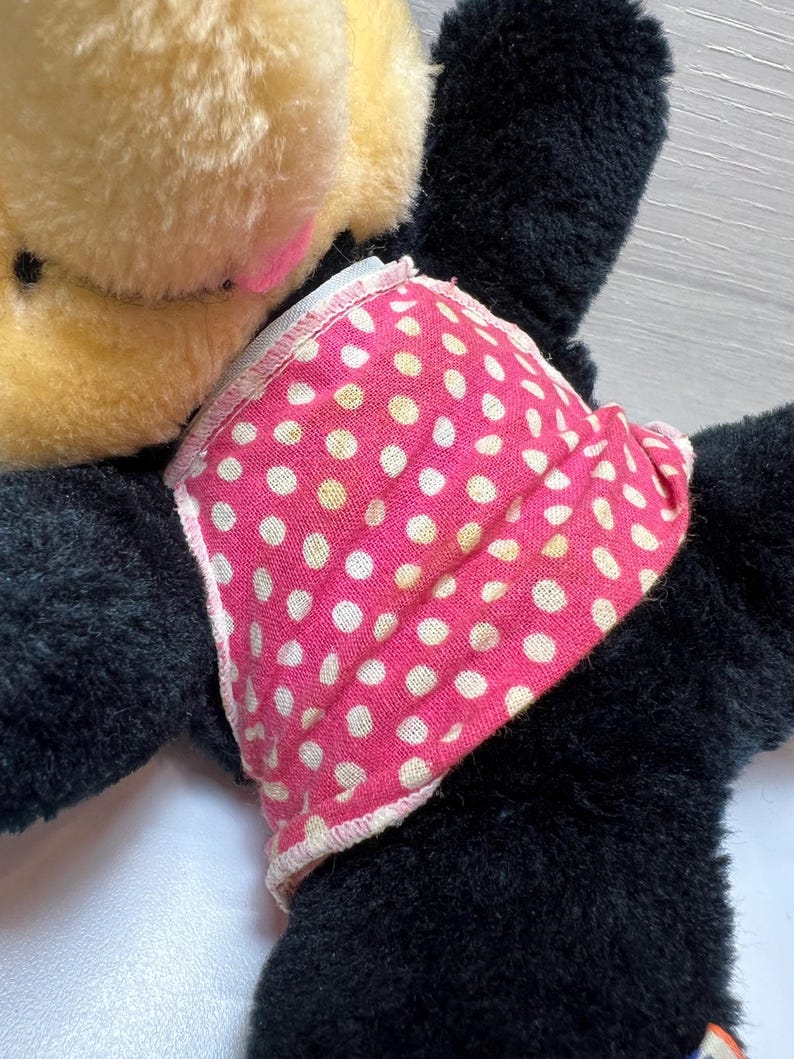 K&ouml;nnte beinhalten: Ein Vintage-Pl&uuml;schtier mit schwarzem K&ouml;rper, beigen Ohren und einem rosa Gesicht. Das Spielzeug tr&auml;gt ein rosa Kleid mit Polka-Dots. Das Pl&uuml;schtier ist weich und scheint sehr geliebt worden zu sein.